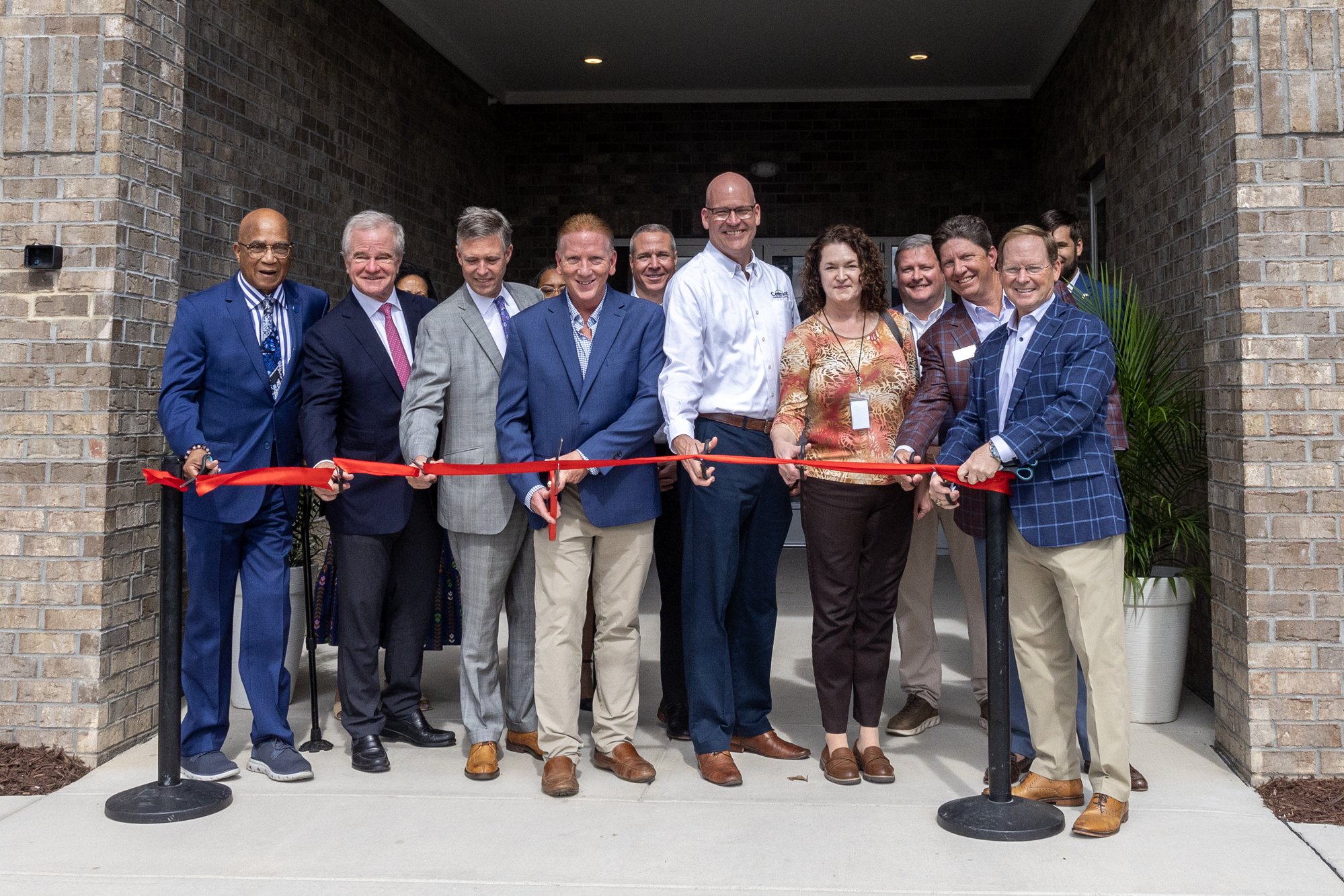 Ribbon cutting at Midtown at BullStreet development. People standing in a row, preparing to cut a red ribbon.