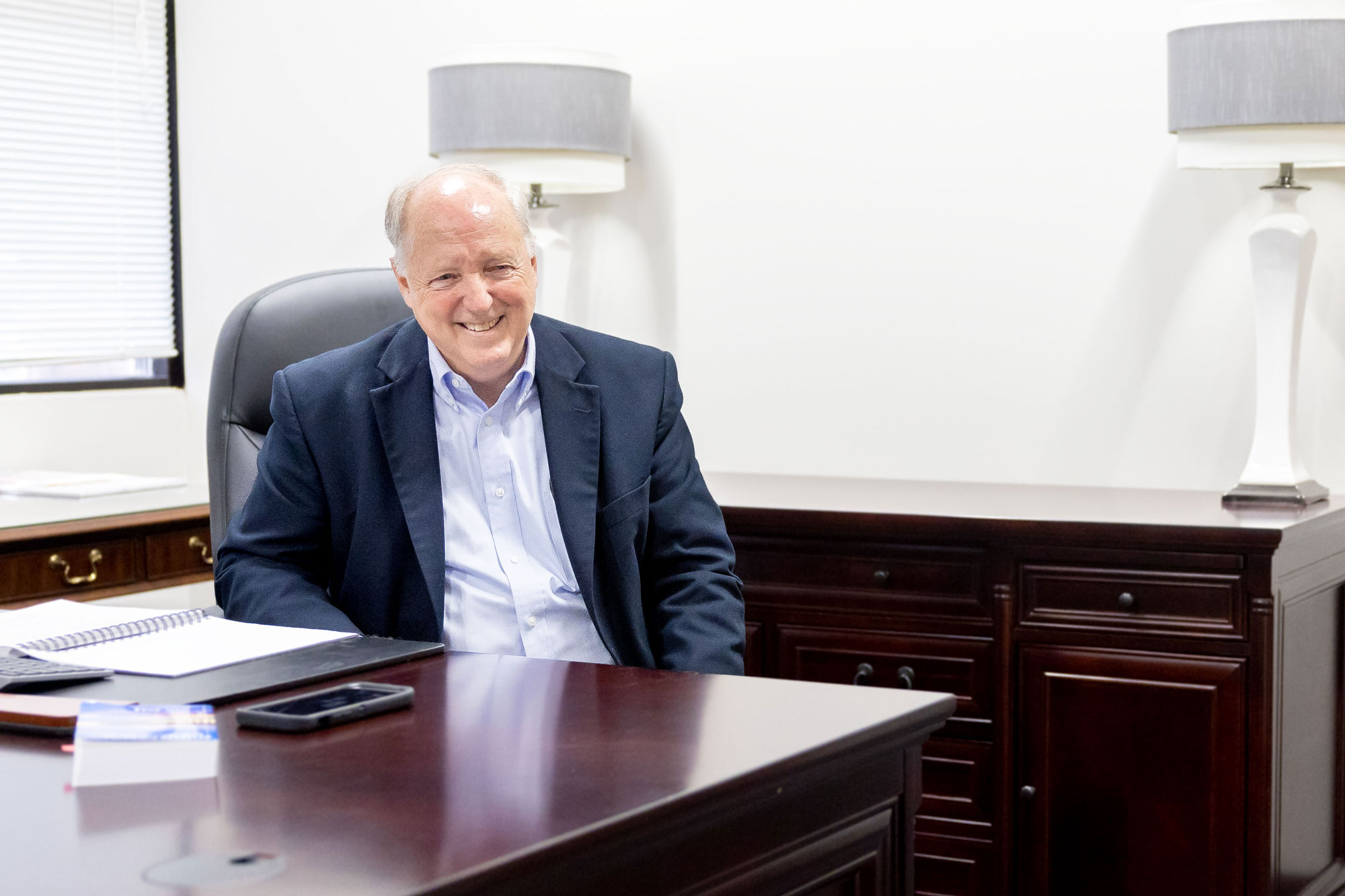 Richard Hutto speaks in his office at SC Housing. He's sitting behind his desk, smiling, wearing a blue coat, a pale blue shirt and is gesturing with his hands.