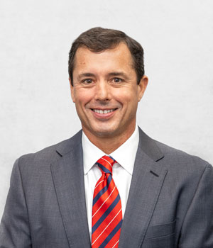 Robert Macdonald posing for a portrait with a grey suit, white shirt and striped red, blue and yellow tie.
